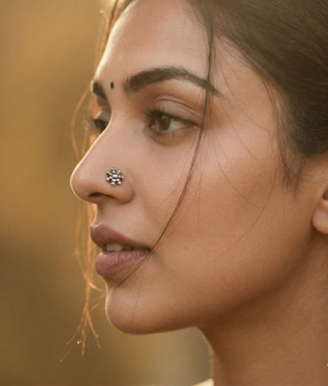 Side profile portrait of a woman with a traditional silver floral nose stud, warm natural lighting, and a soft blurred background.